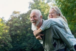 Mature woman piggy-back riding on her husband’s back, both smiling and surrounded by trees